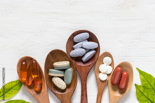 Vitamin capsules in wooden spoons on white wooden background