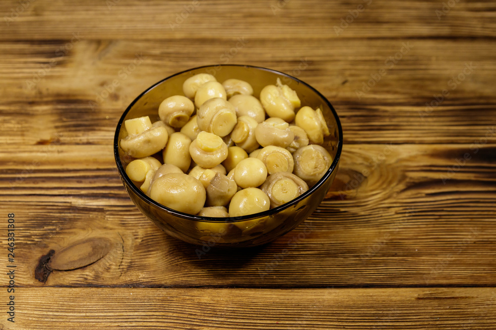 Glass bowl with pickled champignons. Marinated mushrooms on wooden table Glass bowl with pickled champignons. Marinated mushrooms on wooden table