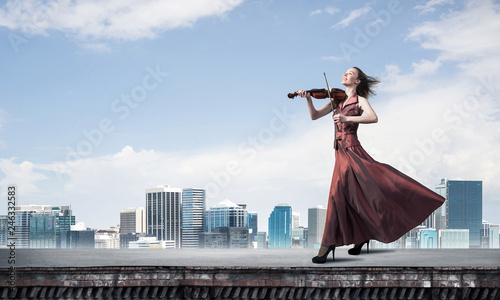 Woman violinist in red dress playing melody against cloudy sky. Mixed media