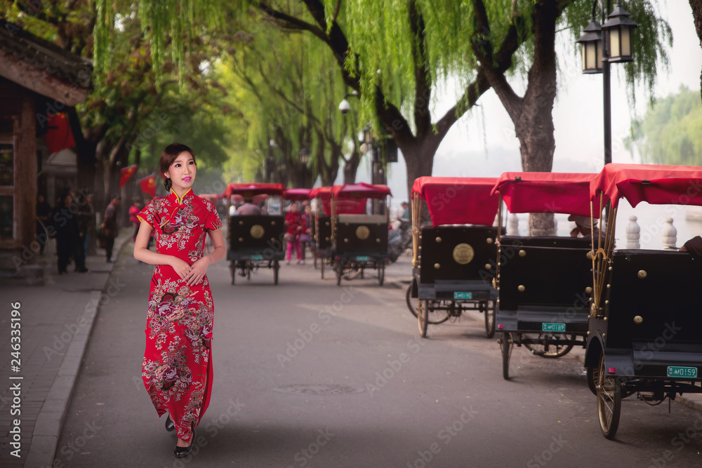Obraz premium Chinese lady in red cheongsam dress walking near a Tourists riding Beijing traditional rickshaw