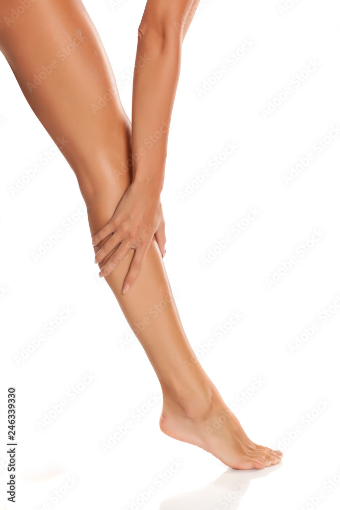 Young woman applying cream on her legs on white background Young woman applying cream on her legs on white background