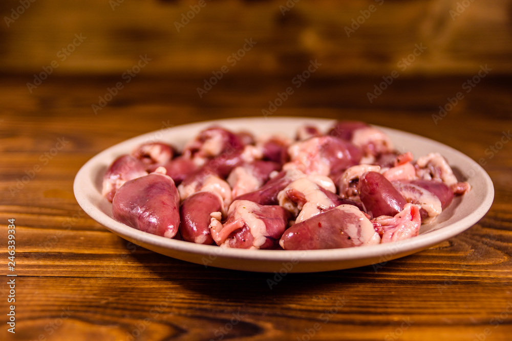 Ceramic plate with raw chicken hearts on wooden table