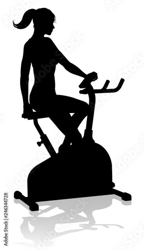 A woman in silhouette using a stationary exercise spin bike piece of gym equipment fitness machine 