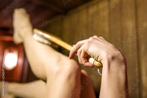 Woman in a sauna massaging her foot with a brush. Beauty spa day concept