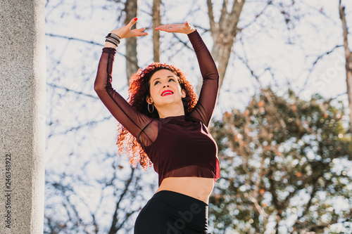 .Young and attractive red haired latin woman dancing urban style on the street on a sunny winter day. Wear sports clothes Positive attitude, happiness. Lifestyle.