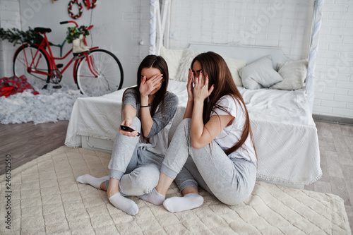 Two twins models girls while click the remote control from the TV on studio and hiding faces, becouse they watched scary movie. They are frightened and shocked. photo