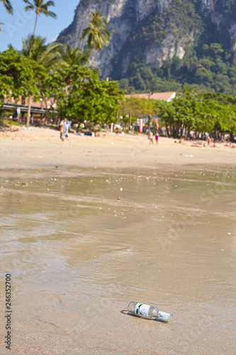 Empty glass bottle left on a beach, tourism development related environment littering concept, Thailand. photo