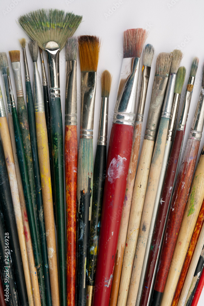Fototapeta premium A collection of well used art paint brushes on white paper surface
