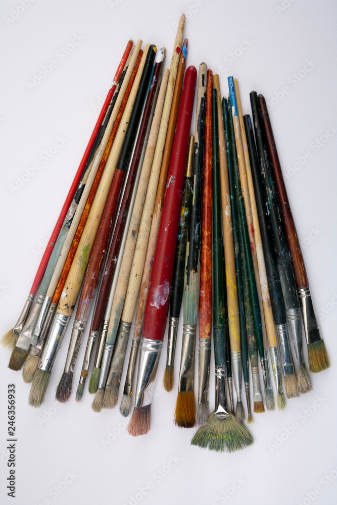 A collection of well used art paint brushes on white paper surface A collection of well used art paint brushes on white paper surface