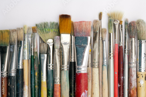A collection of well used art paint brushes on white paper surface
