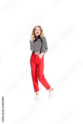 cheerful blonde woman standing with hand in pocket isolated on white
