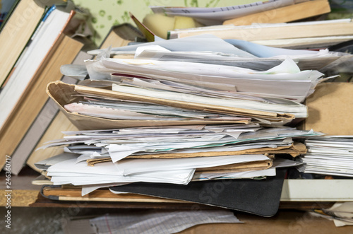 On the shelf are closely stacked pile of folders, papers, books, standing next.