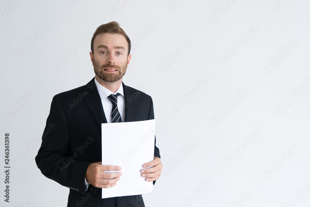 Confused businessman holding papers and grimacing. Frowning shocked young man in suit looking at camera. Entrepreneur concept Confused businessman holding papers and grimacing. Frowning shocked young man in suit looking at camera. Entrepreneur concept