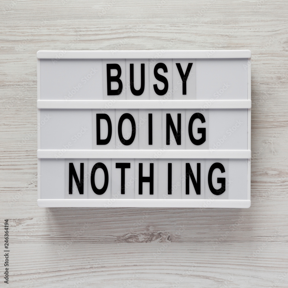 Modern board with text 'Busy doing nothing' on a white wooden surface, top view. From above, flat lay, overhead. Modern board with text 'Busy doing nothing' on a white wooden surface, top view. From above, flat lay, overhead.