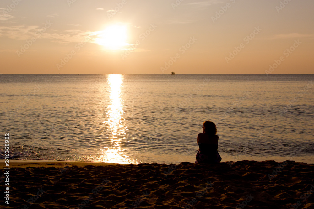 silhouette of a woman sitting on a beach at sunset
