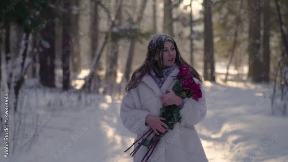 Beautiful young woman walking across winter snowy forest with roses