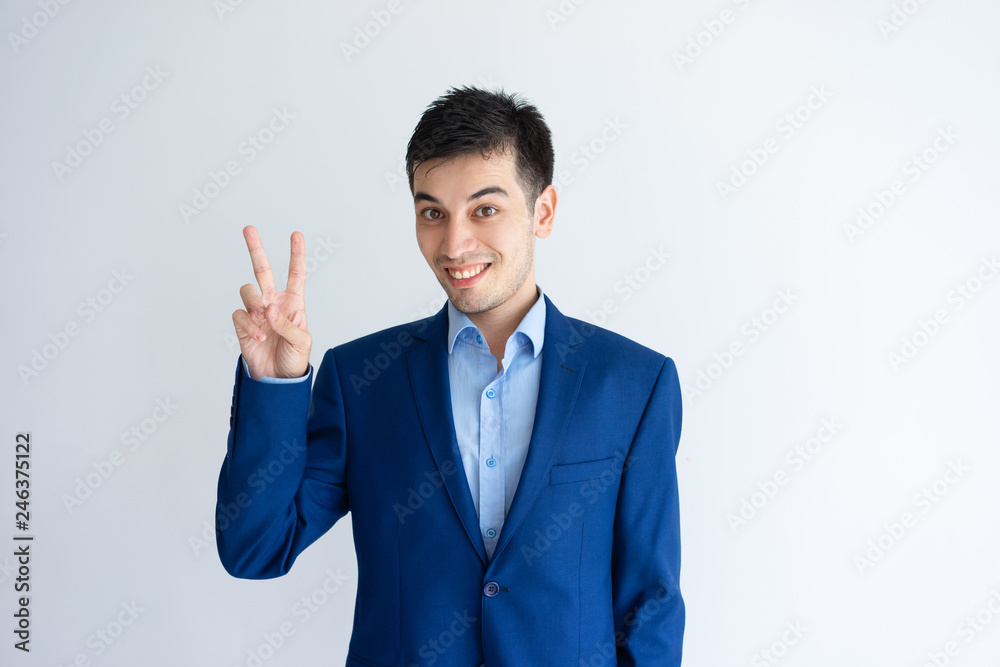 Smiling young business man showing victory sign. Guy looking at camera and celebrating success. Victory concept. Isolated front view on white background. Smiling young business man showing victory sign. Guy looking at camera and celebrating success. Victory concept. Isolated front view on white background.