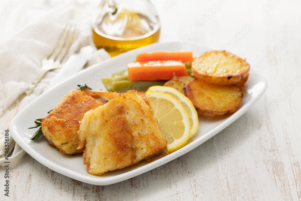 fried cod fish with lemon and vegetables on white plate