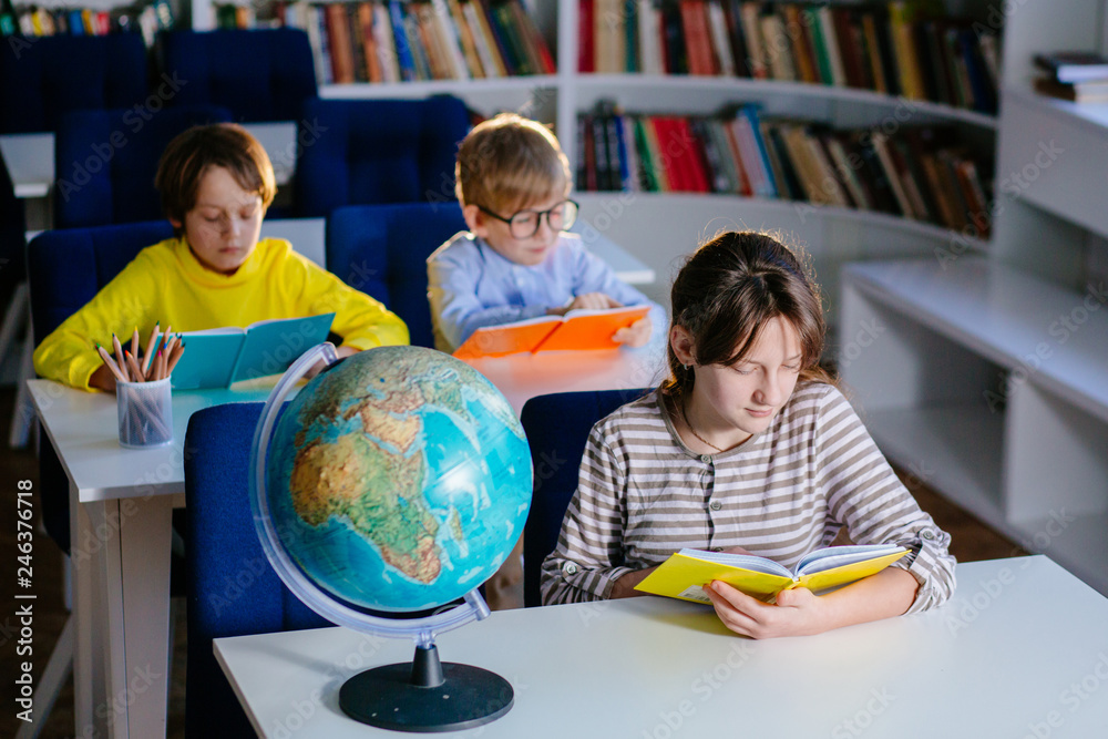 Fototapeta premium Three children reading open books, bright colorful covers. School kids different age studying sitting in class room. Education, elementary school, learning and people concept.