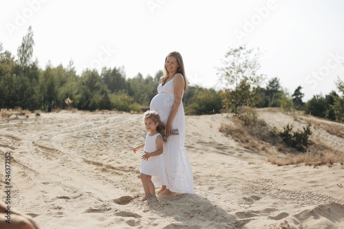 Happy pregnant mother and daughter relaxing on the beach