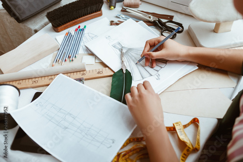 Close-up of young woman tailor with not pad is making sketches