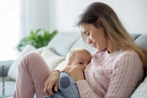 Young mother, holding her sick toddler boy, breastfeeding him at home