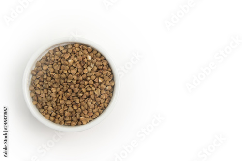 Dry buckwheat in white ceramic bowl isolated on grey table. Spilled buckwheat.