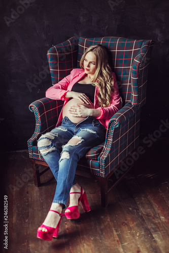 Pregnant woman in dress holds hands on belly on a black background. Pregnancy, maternity, preparation and expectation concept. Close-up, copy space, indoors. Beautiful tender mood photo of pregnancy