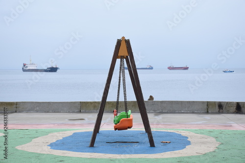 swing in thean empty swing on the shore, sea and ships in the background