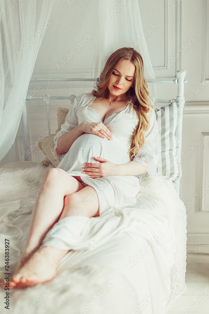 Pregnant woman in dress holds hands on belly on a white background. Pregnancy, maternity, preparation and expectation concept. Close-up, copy space, indoors. Beautiful tender mood photo of pregnancy