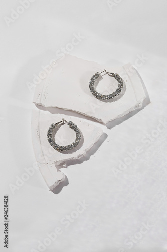 A close up shot of a set of silver earrings adorned with gems. The set is isolated against the white textured platform on the white background. Beautiful accessory for important occasion or a party. photo