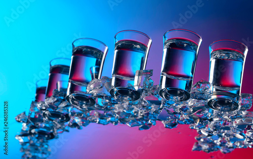 Glasses of vodka with ice on a glass table.