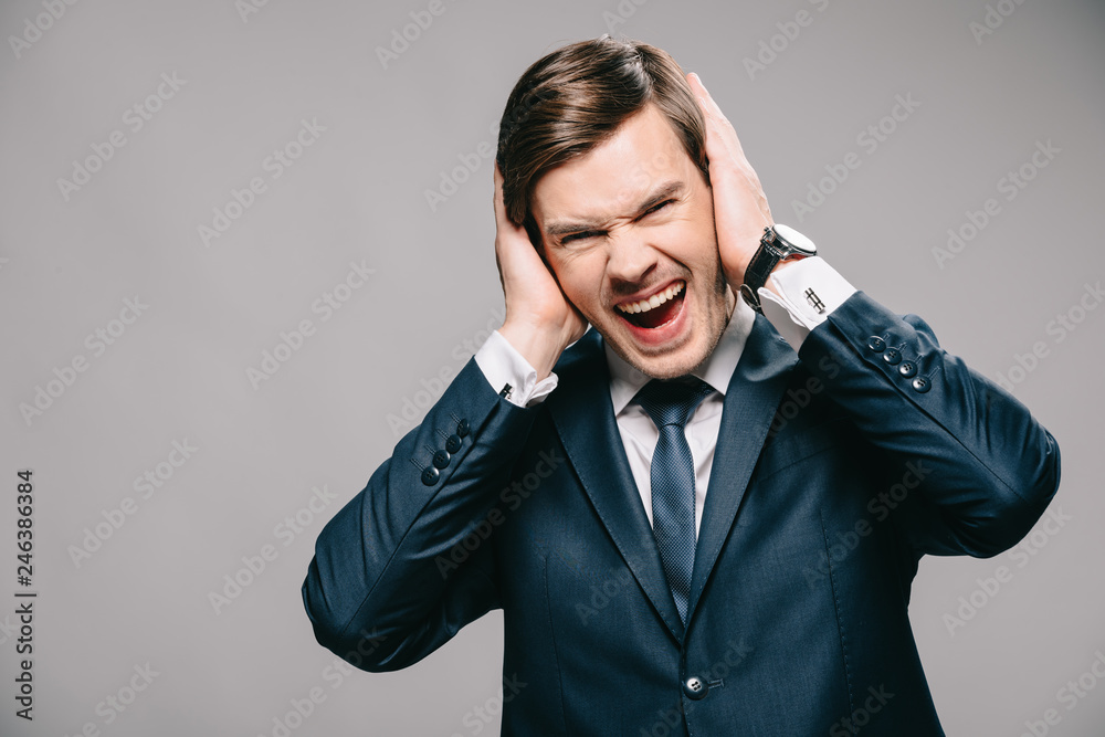 handsome businessman covering ears with hands and screaming on grey background handsome businessman covering ears with hands and screaming on grey background