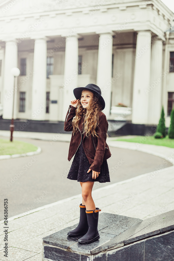 Outdoor portrait of teenage girl in stylish look, in black hat posing outdoors in park