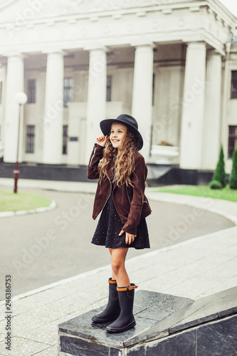Outdoor portrait of teenage girl in stylish look, in black hat posing outdoors in park