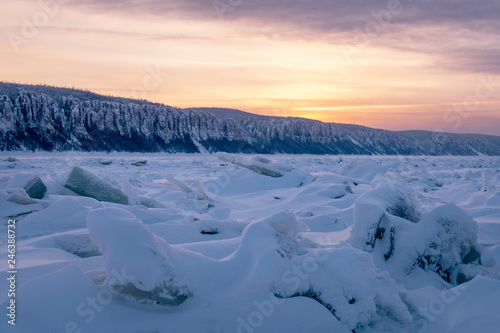 Winter landscape in pink tones with ridged ice on the frozen Lena river at sunset in the Natural Park Lenskie Stolby (Lena Pillars), Yakutia, Russia