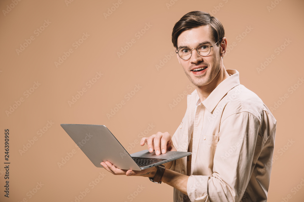 handsome man in glasses using laptop isolated on beige