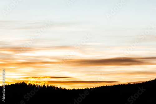 Golden stratus clouds above mountain silhouette. Sunset in mountain valley