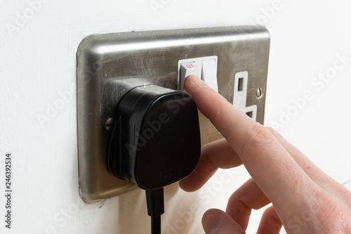 Stainless steel UK plug socket on white wall with hand switching on photo