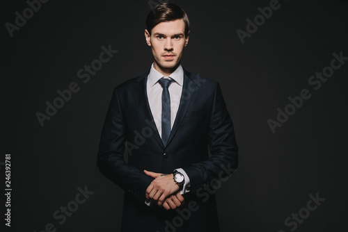 handsome and confident man standing in suit isolated on black