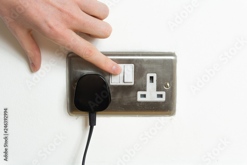 Stainless steel UK plug socket on white wall with hand switching on