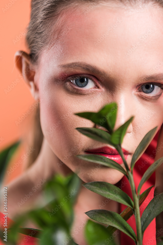 portrait of beautiful stylish girl looking at camera and posing with plant isolated on living coral portrait of beautiful stylish girl looking at camera and posing with plant isolated on living coral