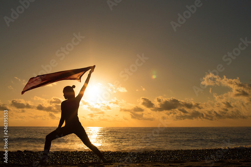 Silhouette of woman with waving flag in hand by the sea at sunset.