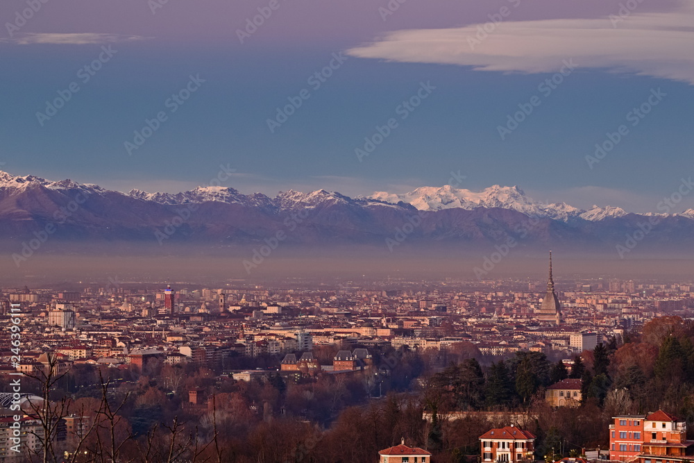 Panorama of Turin at dawn, overlooking the city center and the Mole Antonelliana, a backdrop of snow-capped mountains illuminated by pink light