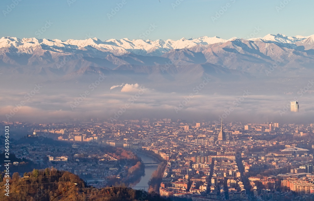 Obraz premium Panoramic view at sunrise on Turin city seen from Superga in winter, with a layer of smog that falls on buildings, snowy Alps mountains on background