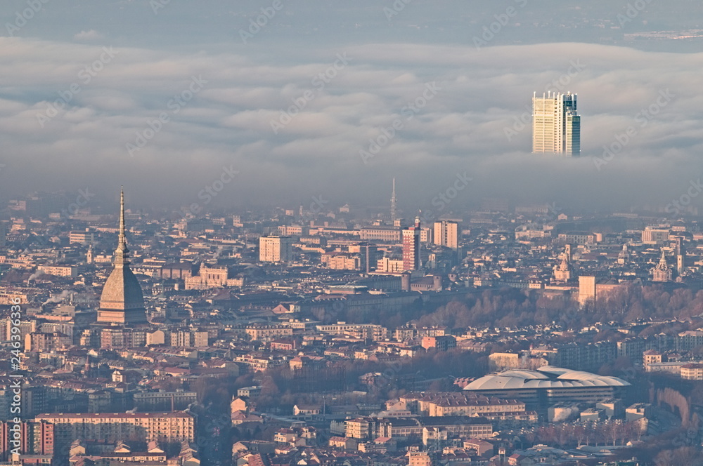 Panoramic view at sunrise on Turin city seen from Superga in winter, with a layer of smog that falls on buildings, snowy Alps mountains on background