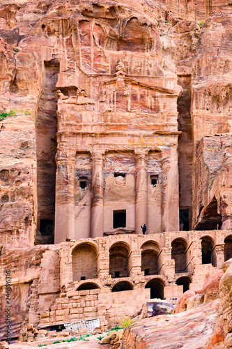 A man take pictures in front of a huge temple carved into the rock in Petra.