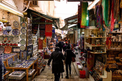 Some people walk through the streets of the old city of Jerusalem with stalls and shops selling souvenirs and food. 