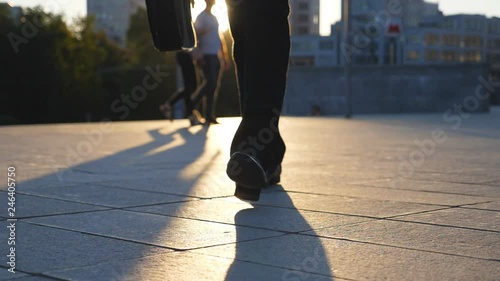 Feet of businessman with briefcase walking in city street at sunset time. Businessman commuting to work. Confident guy being on his way to office. Worker going outdoor. Front view Close up Slow motion photo