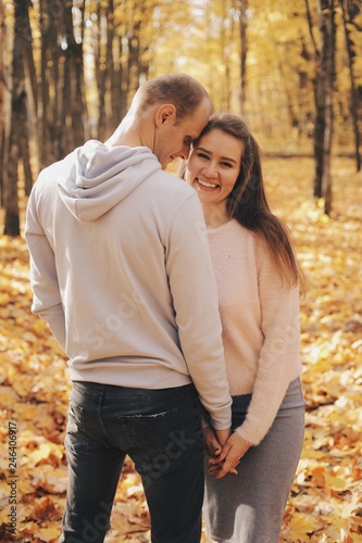 Couple stands in the forest together. Attractive girl hugging her boyfriend and looking at the camera. Happy family stay in autumn park.